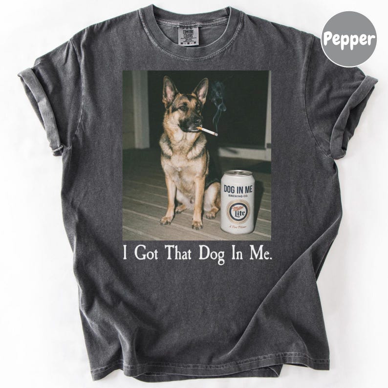 A German Shepherd dog sitting on a wooden floor next to a can of Miller Lite beer, with the text "I Got That Dog In Me."