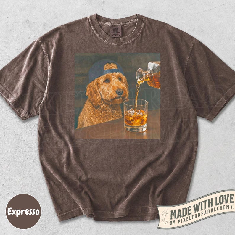 K&ouml;nnte beinhalten: Braunes T-Shirt mit einem Aufdruck eines Hundes mit Baseballkappe, der dabei zusieht, wie Whiskey in ein Glas gegossen wird. Der Hund hat braunes Fell. Das T-Shirt hat einen Vintage-Look. Der Text "Made with Love" ist sichtbar.