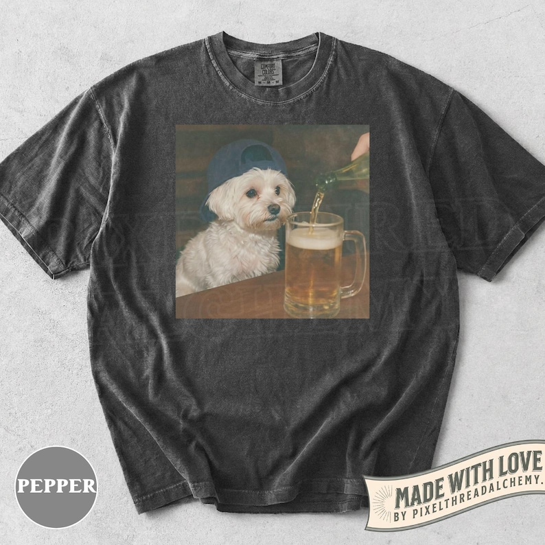 May include: Dark gray t-shirt featuring a graphic of a white dog wearing a blue baseball cap, sitting at a table while beer is poured into a mug. The shirt has a vintage, washed look. The text "MADE WITH LOVE" is visible.