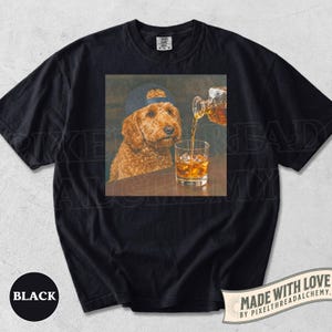 K&ouml;nnte beinhalten: Schwarzes T-Shirt mit einem quadratischen Aufdruck, der einen Hund mit Baseballkappe zeigt, in den Whisky gegossen wird. Auf dem Shirt steht auch das Wort "BLACK".