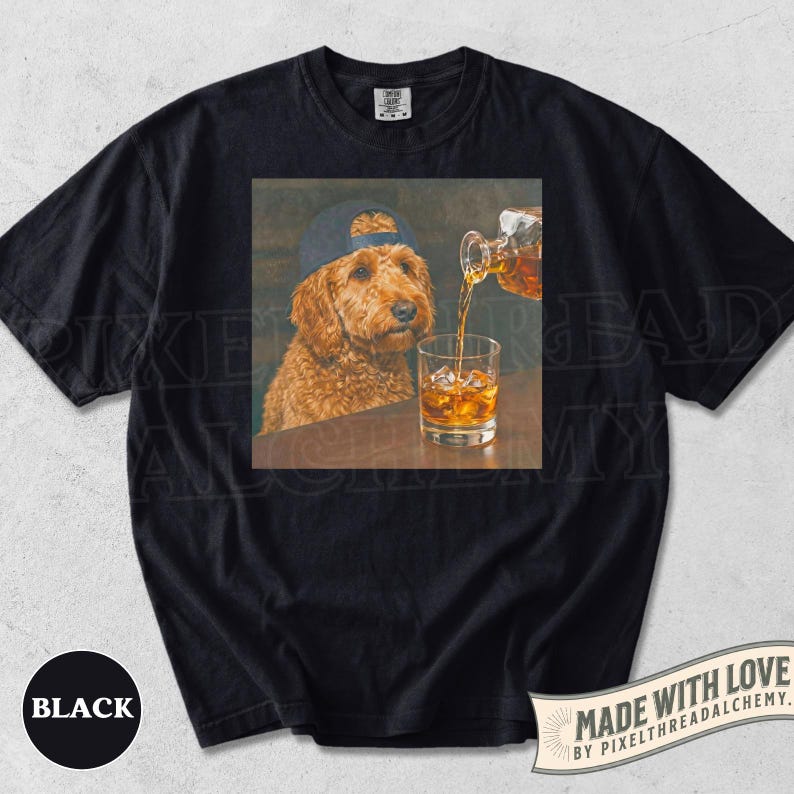 K&ouml;nnte beinhalten: Schwarzes T-Shirt mit einem quadratischen Aufdruck, der einen Hund mit Baseballkappe zeigt, in den Whisky gegossen wird. Auf dem Shirt steht auch das Wort "BLACK".