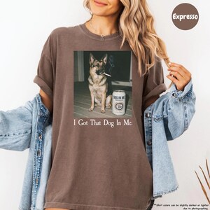 A woman wearing a brown t-shirt with a graphic of a dog smoking a cigarette and the text "I Got That Dog In Me" printed on it.