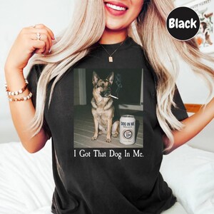 A woman wearing a black t-shirt with a graphic of a dog smoking a cigarette and the text "I Got That Dog In Me."