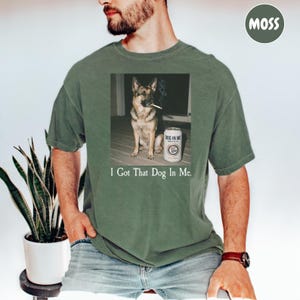A man wearing a green t-shirt with a graphic of a dog smoking a cigarette and a can of beer, accompanied by the text "I Got That Dog In Me."