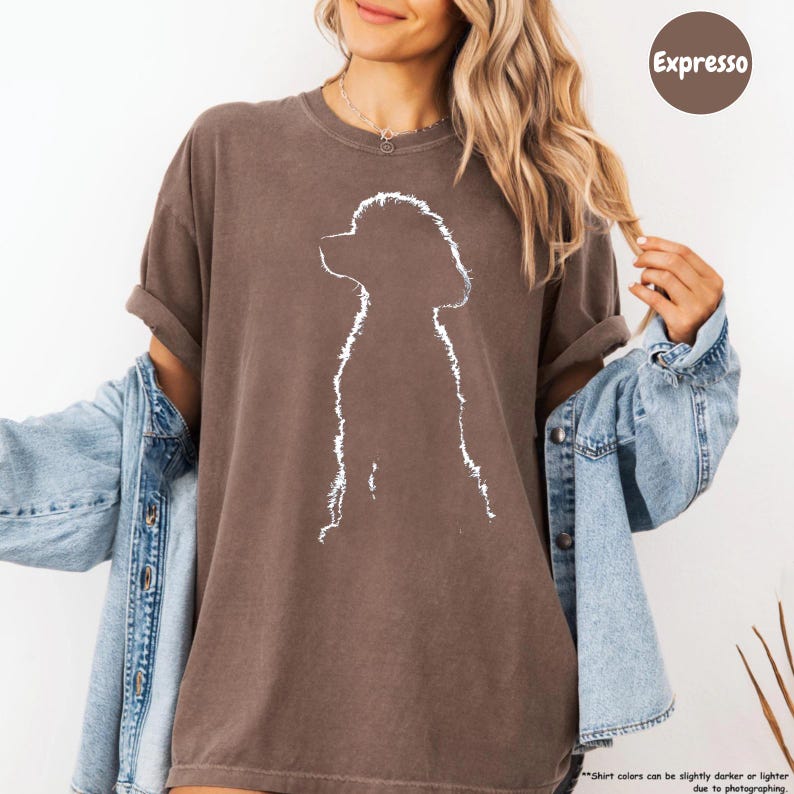 A woman wearing a brown t-shirt with a white silhouette of a dog, paired with a denim jacket, posing against a white background.