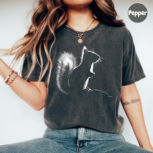 A woman wearing a gray t-shirt with a white silhouette of a squirrel printed on it, paired with blue jeans.