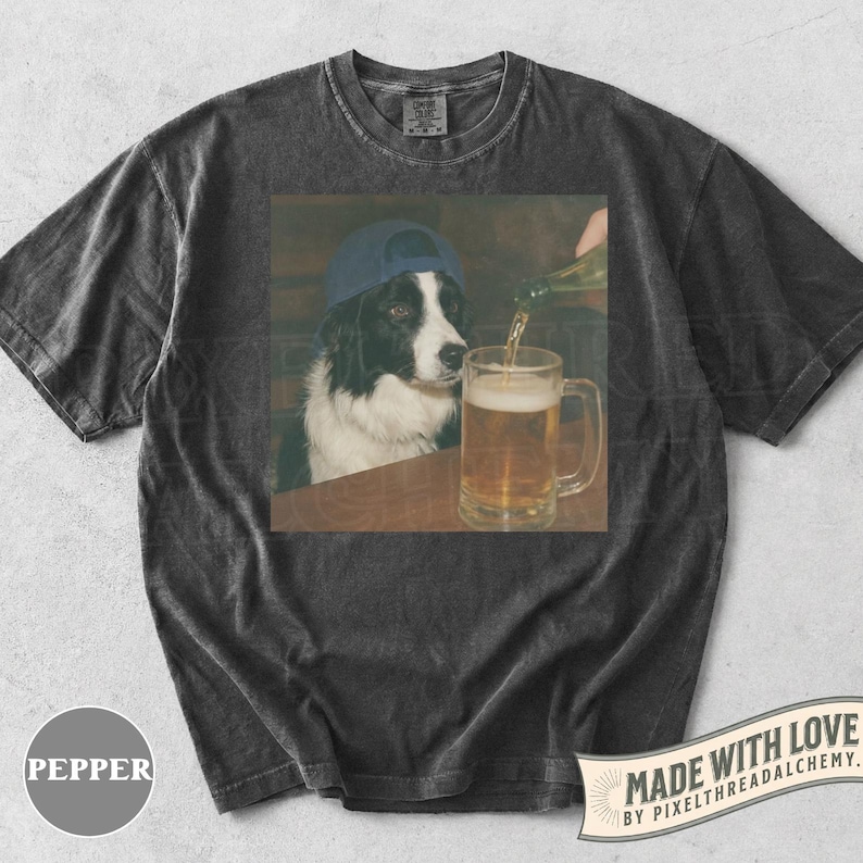 May include: Dark grey t-shirt with a graphic of a Border Collie wearing a blue cap, watching a beer mug being filled. The shirt has the word "PEPPER" printed on the bottom left and "MADE WITH LOVE" on the bottom right.