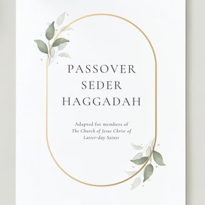 May include: A white card with a gold oval frame and green watercolor leaves. The text inside the frame reads "Passover Seder Haggadah" and "Adapted for members of The Church of Jesus Christ of Latter-day Saints".