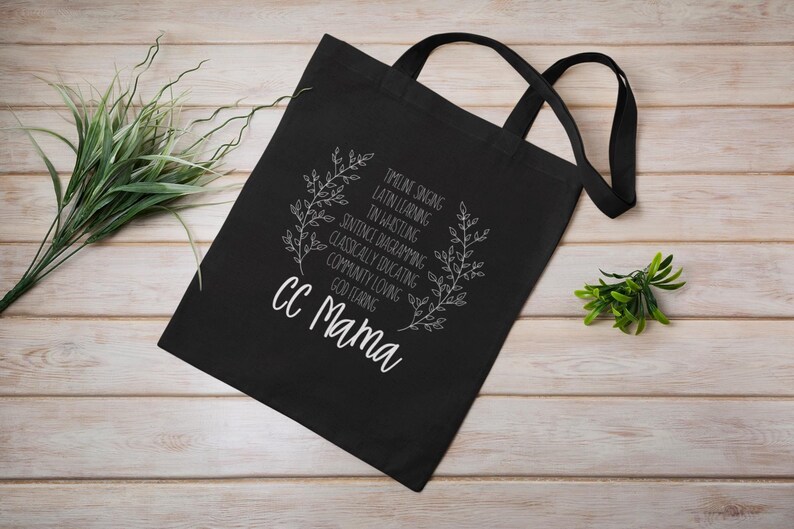 May include: Black tote bag with white text and a floral design. The text reads "TIMELINE SINGING, LATIN LEARNING, IN WHISTLING, SENTENCE DIAGRAMMING, CLASSICALLY EDUCATING, COMMUNITY LOVING, GOD FEARING, CC Mama".
