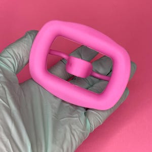 Peut inclure: Un chouchou en silicone rose avec un design unique. Le chouchou a une grande boucle d'un côté et une petite boucle de l'autre, créant une forme unique.