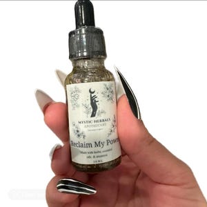 Op de afbeelding: Een glazen fles met een zwarte druppelaar en een wit etiket met de tekst "MYSTIC HERBALS APOTHECARY Reclaim My Power Made with herbs, essential oils & intention 10ML".
