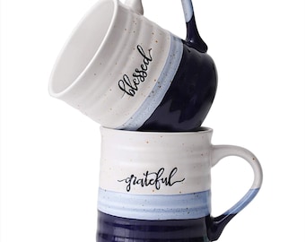 Può includere: Due tazze in ceramica impilate l'una sull'altra. La tazza superiore è bianca con accenti blu e dorati e dice "blessed" in scrittura nera. La tazza inferiore è bianca con accenti blu e dorati e dice "grateful" in scrittura nera.