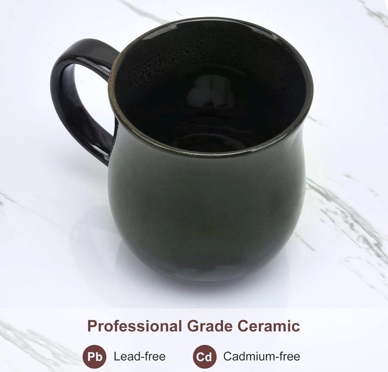May include: A dark green ceramic mug with a glossy finish and a curved handle. The text below the mug reads: Professional Grade Ceramic, Pb Lead-free, and Cd Cadmium-free. The mug has a rounded body and a smooth, reflective surface texture.