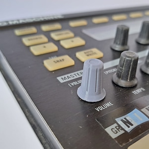 May include: A close-up of a grey knob on a black music production controller. The knob is labelled "Volume" and is next to a sticker that says "GR NI" and "NATIVE INSTRUMENTS".