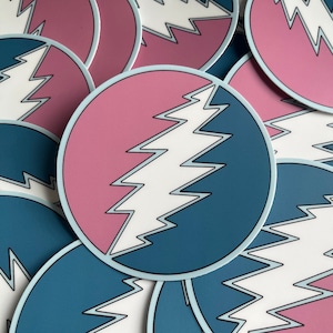May include: A stack of round stickers with a white lightning bolt design on a pink and blue background.