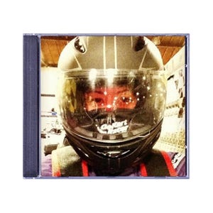 May include: A black and gray Go Kart Racer helmet with a clear visor. The helmet is in a CD case. The visor reflects the image of a person wearing the helmet. The text "Go Kart Racer" is visible on the helmet.