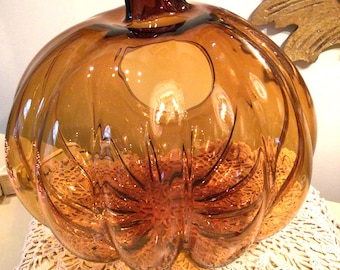 May include: A large amber glass pumpkin with a deep brown stem. The pumpkin is sitting on a white crocheted doily.