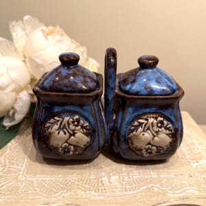 May include: A set of three ceramic mugs with a speckled, matte finish. Each mug features a different color: light blue, cream, and gray. The mugs have a simple, modern design and a comfortable handle.