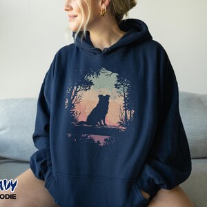 May include: Navy blue hoodie with a dog silhouette set in a natural scene, including trees and a colourful sky. The text "NAVY HOODIE" is printed at the bottom left corner of the image.