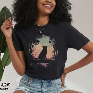 May include: Black t-shirt with a dog silhouette in a forest scene against a sunset backdrop. The text "BLACK T-SHIRT" is printed in white. The shirt is made of a soft material. The design evokes a sense of nature and tranquility.