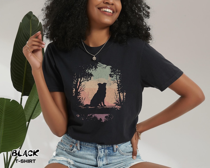 May include: Black t-shirt with a dog silhouette in a forest scene against a sunset backdrop. The text "BLACK T-SHIRT" is printed in white. The shirt is made of a soft material. The design evokes a sense of nature and tranquility.