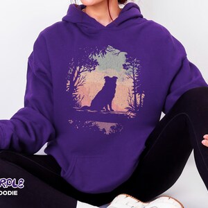 May include: A purple hooded sweatshirt with a dog silhouette in a forest scene against a sunset. The text "PURPLE HOODIE" is at the bottom left of the image.