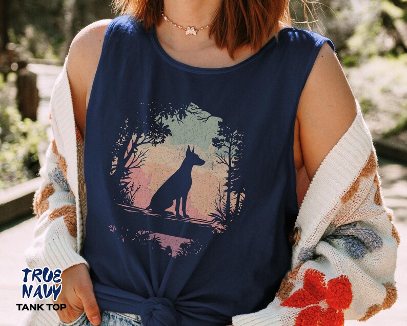 Pu&ograve; includere: Canotta blu navy con la silhouette di un cane in una scena di foresta. La grafica presenta un cane seduto in una foresta con uno sfondo colorato del tramonto. Il testo "TRUE NAVY TANK TOP" &egrave; stampato in basso a sinistra.