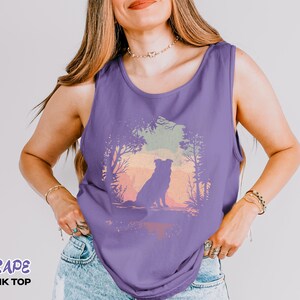 May include: A sleeveless grape-coloured tank top with a dog silhouette set against a sunset landscape. The text "GRAPE TANK TOP" is printed at the bottom. The tank top is made of a soft material and is suitable for warm weather.