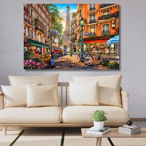 May include: A colourful painting depicting a Parisian street scene with a woman cycling past a bakery called "Boulangerie Patisserie". The Eiffel Tower can be seen in the background.