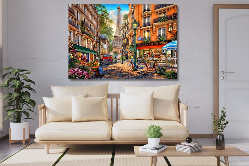 May include: A colourful painting depicting a Parisian street scene with a woman cycling past a bakery called "Boulangerie Patisserie". The Eiffel Tower can be seen in the background.