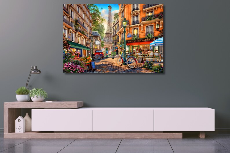 May include: A colourful painting depicting a Parisian street scene with a flower shop, a bakery called "Boulanger Patissier", and a bicycle. The Eiffel Tower can be seen in the background.