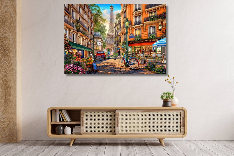 May include: A colourful painting depicting a Parisian street scene with a flower shop, a bakery called "Boulanger Patissier", and a person riding a bicycle. The Eiffel Tower can be seen in the distance.