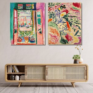 May include: Two colourful abstract paintings, one depicting a window with a view of a harbour and the other depicting a woman in a landscape. The paintings are framed and hung on a white wall above a wooden cabinet.