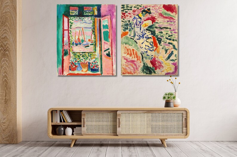 May include: Two colourful abstract paintings, one depicting a window with a view of a harbour and the other depicting a woman in a landscape. The paintings are framed and hung on a white wall above a wooden cabinet.