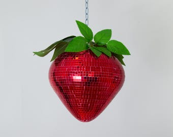 May include: A red, mosaic strawberry-shaped hanging ornament with green leaves. The ornament is made of small, mirrored tiles and hangs from a silver chain.