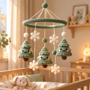 May include: A hanging nursery mobile featuring three crocheted green Christmas trees with smiling faces and pink cheeks, interspersed with white crocheted snowflakes and small green and white spheres, all suspended from a circular green crocheted frame.