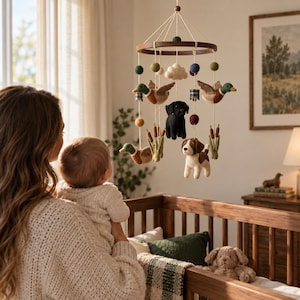 May include: A hanging nursery mobile featuring a circular wooden frame with suspended felt figures including two mallard ducks, a black Labrador, a beagle, cattails, a white cloud, and small felt balls in green, blue, and yellow colors.