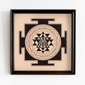 May include: A framed print of a black and white Sri Yantra, a sacred geometric symbol in Hinduism, with a peach-colored background.