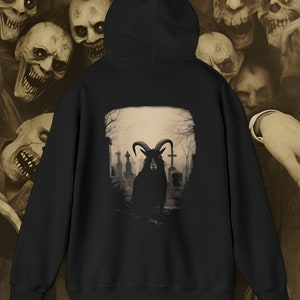 May include: Black hooded sweatshirt with a graphic print of a black goat with horns standing in a graveyard. The goat is facing away from the viewer. The background is a sepia toned image of a graveyard.