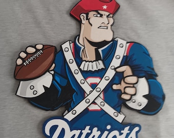 May include: A wooden cutout of the New England Patriots mascot, a colonial-era man in a red hat, blue coat, and white accents, holding a football. The word "Patriots" is written in blue and white below the figure.