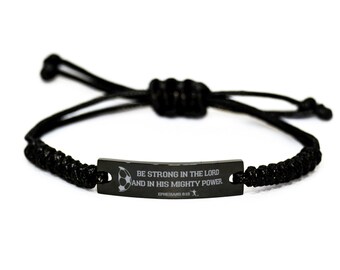 Op de afbeelding: Een zwarte koordarmband met een centrale rechthoekige metalen plaat met een matzwarte afwerking. De plaat is gegraveerd met een voetbalicoon en de tekst BE STRONG IN THE LORD AND IN HIS MIGHTY POWER EPHESIANS 6:10 met een voetballer.