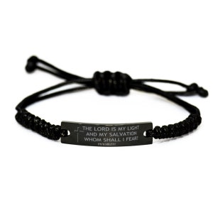 Puede incluir: Pulsera de cordón trenzado negro con una placa rectangular de metal oscuro. La placa presenta el texto "THE LORD IS MY LIGHT AND MY SALVATION WHOM SHALL I FEAR? PSALMS 27:1" y un pequeño símbolo de cruz. La pulsera es ajustable.