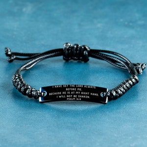 Può includere: Braccialetto nero intrecciato con una placca metallica rettangolare. La placca presenta l'incisione: "I HAVE SET THE LORD ALWAYS BEFORE ME. BECAUSE HE IS AT MY RIGHT HAND. I WILL NOT BE SHAKEN. PSALM 16:8". Il braccialetto è regolabile.