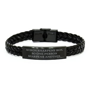 May include: Black braided leather bracelet with a stainless steel clasp. The bracelet features a rectangular plate with the engraved text: "AS IRON SHARPENS IRON, SO ONE PERSON SHARPENS ANOTHER." The text is from Proverbs 27:17.