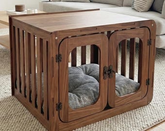May include: A rectangular wooden pet crate with vertical slats and double front doors featuring dark metal hinges and a latch. Inside the crate sits a thick, tufted gray fabric cushion. The structure is made of a medium-toned wood with a smooth finish.