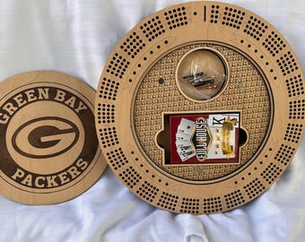 May include: A wooden cribbage board with a circular design, featuring a storage compartment with a deck of cards labeled "FULL HOUSE". The board has a lid with the Green Bay Packers logo.