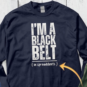 May include: Navy blue long-sleeved t-shirt with white text that reads "I'm a black belt (in spreadsheets)". The shirt is customizable.