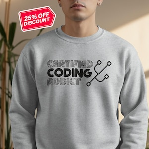 Peut inclure: Sweat-shirt gris sport avec le texte "CERTIFIED CODING ADDICT" et un graphique stylisé. Un autocollant rouge et blanc "25% OFF DISCOUNT" est dans le coin supérieur gauche. Le sweat-shirt est de couleur gris clair.