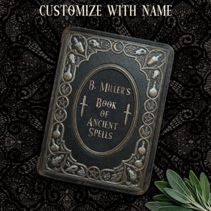 May include: A black, rectangular book with silver embellishments and the text "B. Miller's Book of Ancient Spells." The cover features an oval design with two daggers and decorative elements, including potion bottles and skulls. The text "Customize with Name" is at the top.