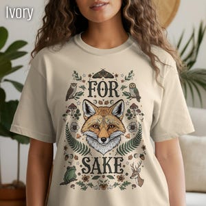 May include: Ivory-colored t-shirt featuring a detailed illustration of a fox's face surrounded by woodland elements. The text "FOR SAKE" is arched above and below the fox. The design includes owls, mushrooms, and a deer.